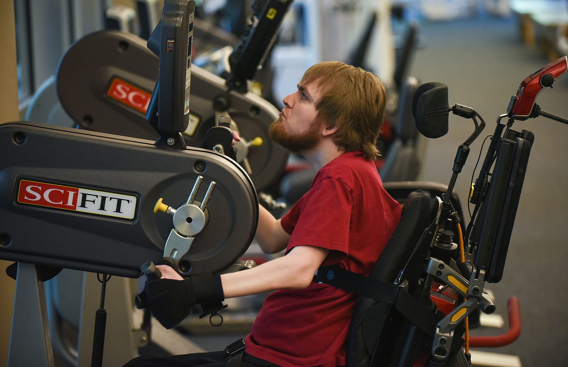 Man in wheelchair pulling up weights in gym